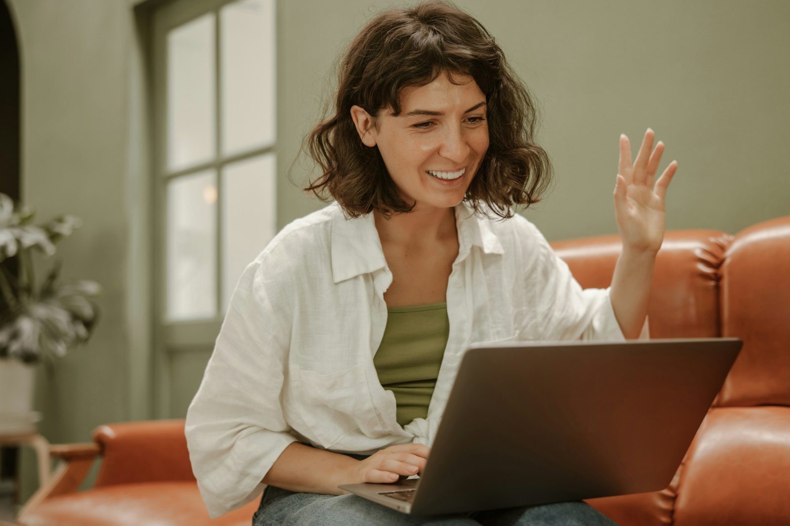 A patient on the couch at home, waving to their doctor on a laptop